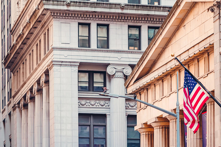 Featured Image: Neoclassical architecture of lower Manhattan, Wall Street buildings with American flag flying